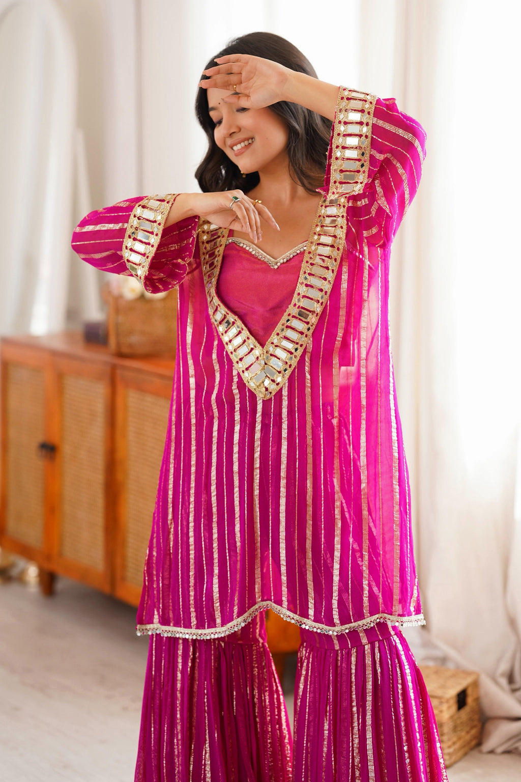 Pink sharara suit close-up showing gold zari detailing and mirror-work neckline