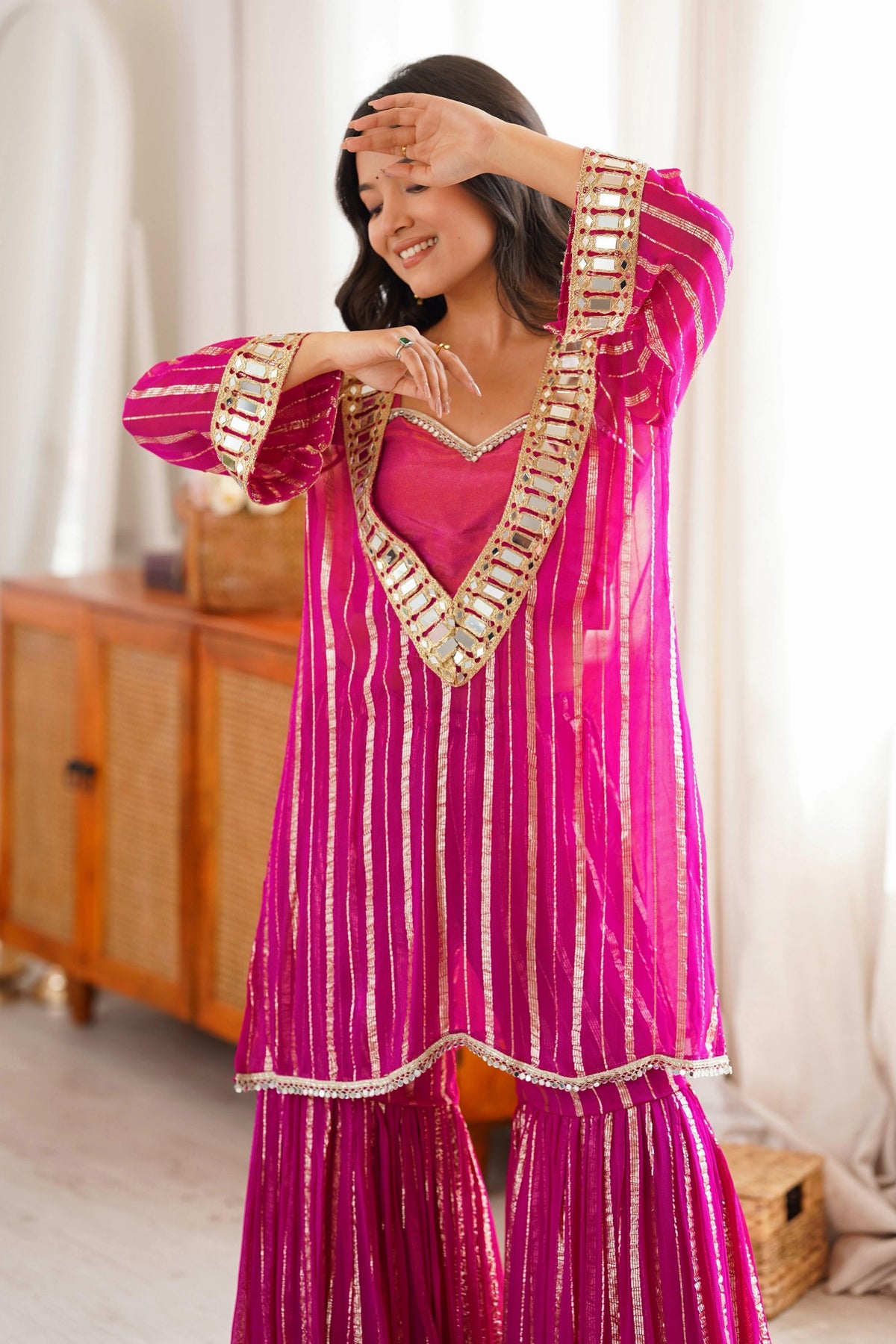 Pink sharara suit close-up showing gold zari detailing and mirror-work neckline