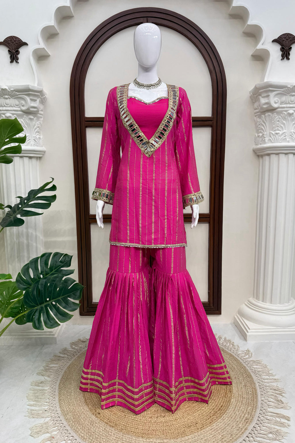 Pink sharara suit displayed on mannequin with gold zari stripes and detailed borders