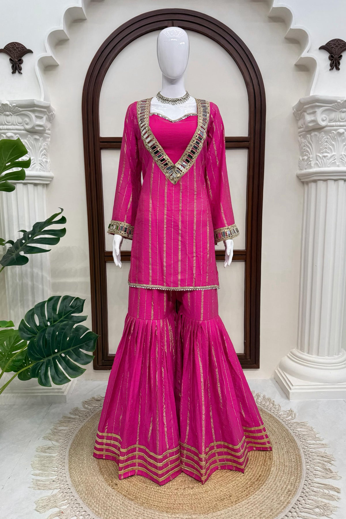 Pink sharara suit displayed on mannequin with gold zari stripes and detailed borders