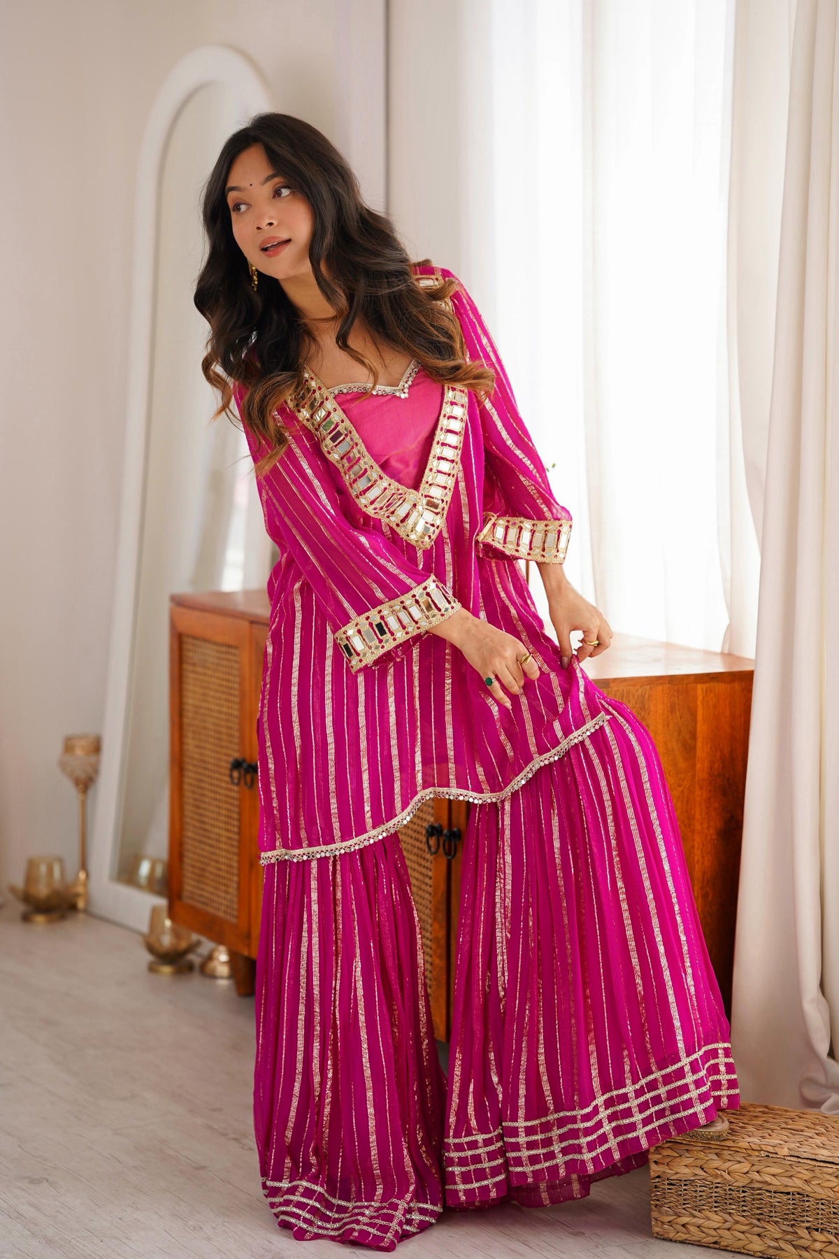 Pink sharara suit with real mirror work and gold zari detailing styled on a model