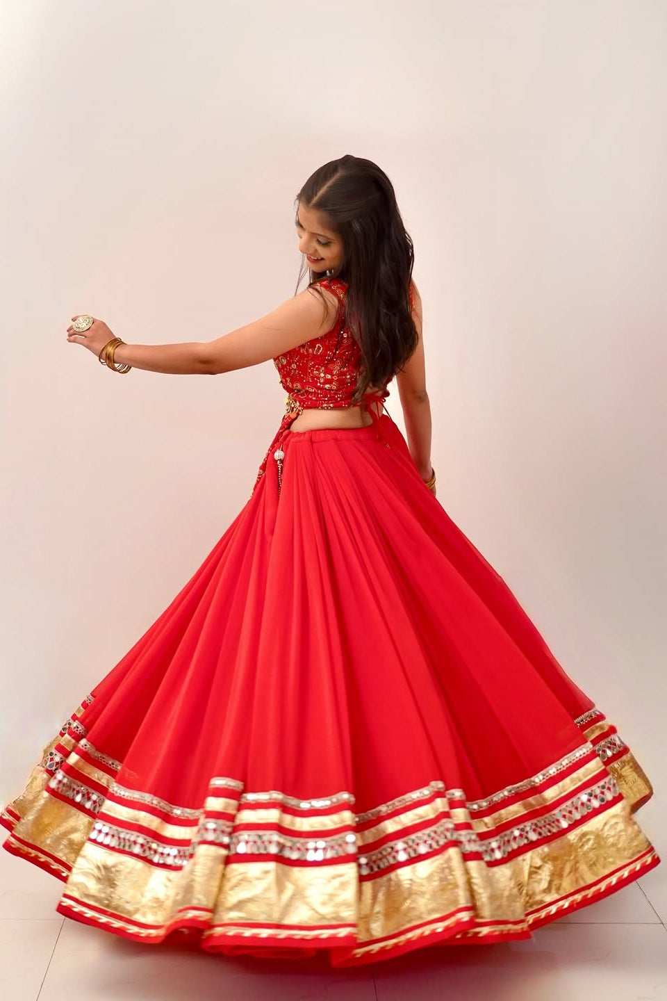 Back twirl view of red lehenga choli showing its wide flowing silhouette and gold border