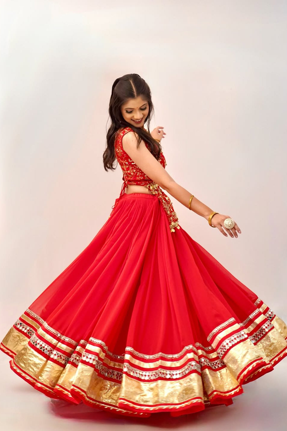 Side view of red festive lehenga choli displaying the flowing skirt and gold lace border