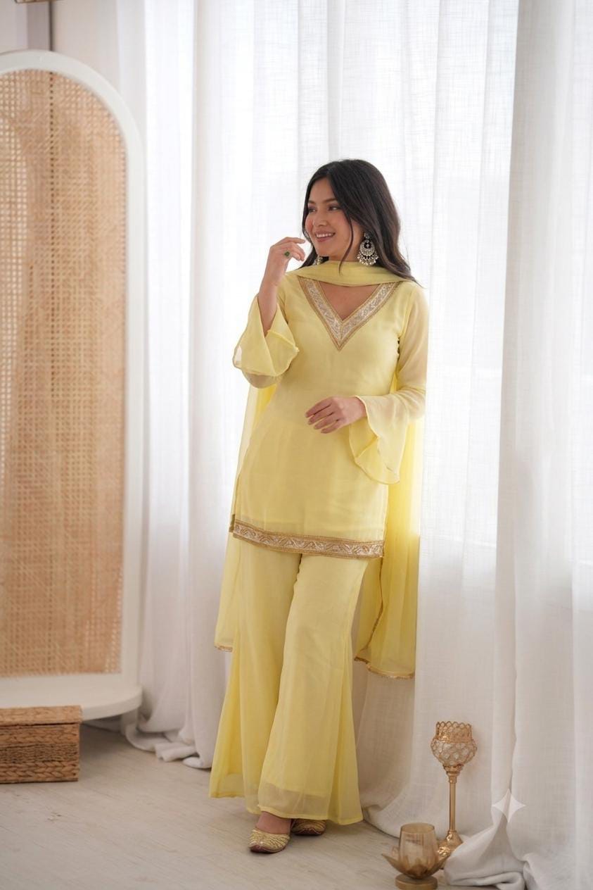 Model posing indoors in yellow embroidered palazzo suit set near sheer curtains